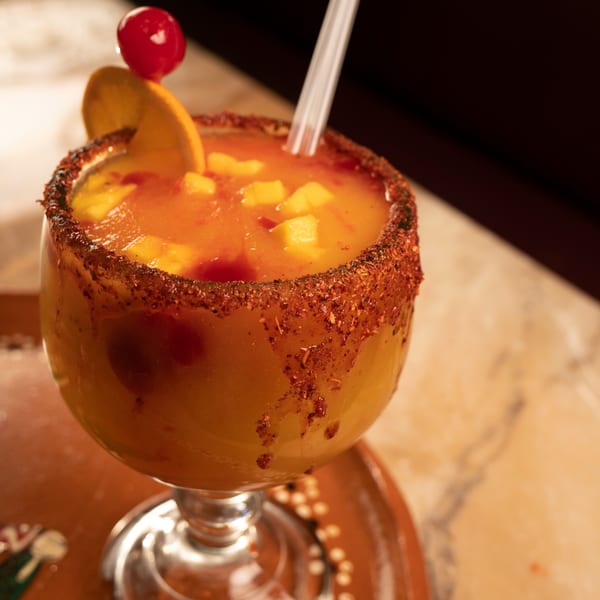 A mango margarita with a chili-lime rim, garnished with an orange slice and cherry, from Amigos Mexican Cuisine.