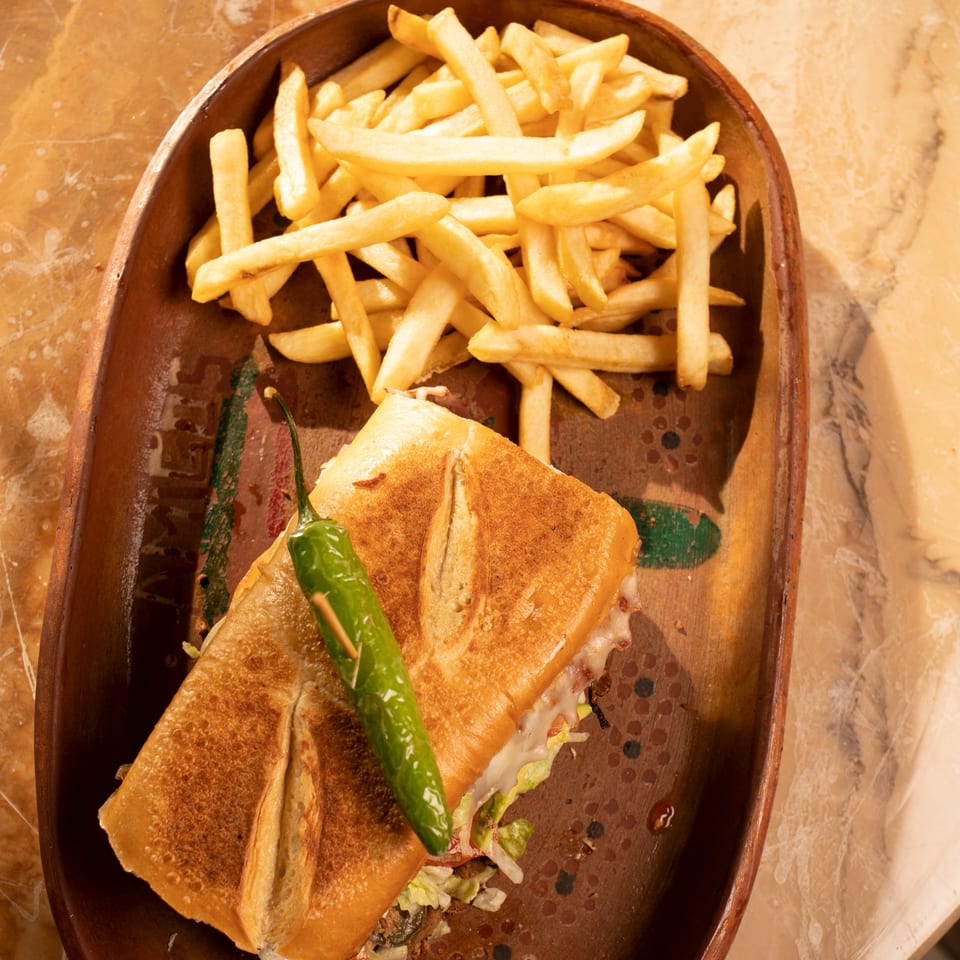 Amigos Mexican Cuisine's torta sandwich with a green chili and a side of golden french fries.