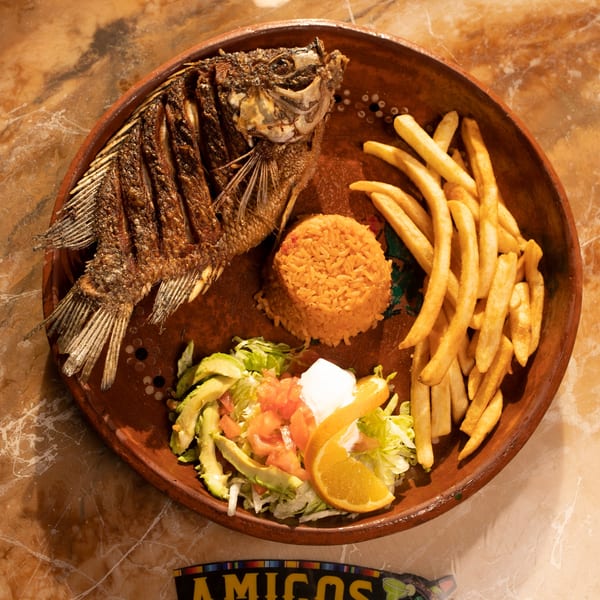 Whole fried fish with rice, french fries, and a side salad on a rustic plate at Amigos Mexican Cuisine.