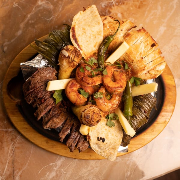A sizzling platter of Amigos Mexican Cuisine fajitas with steak, shrimp, peppers, onions, and tortillas.