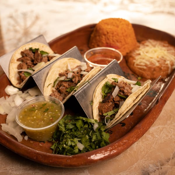 Three Amigos Mexican Cuisine tacos with rice, beans, salsa, and cilantro on a rustic tray.